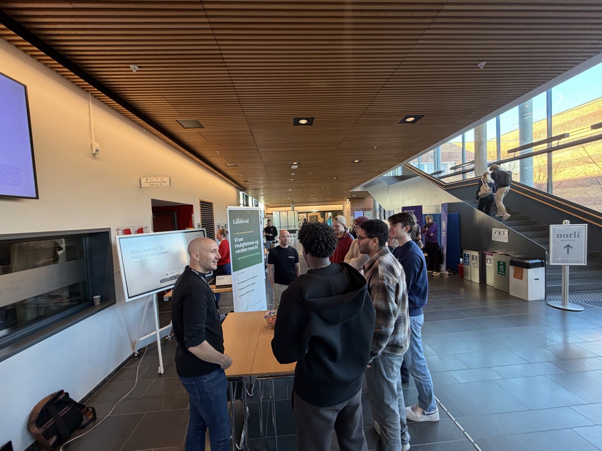 Studenter i samtale ved Lillehvals stand på USN Bakkenteigen, med roll-upen «Vi ser mulighetene og verdien med AI» i bakgrunnen.